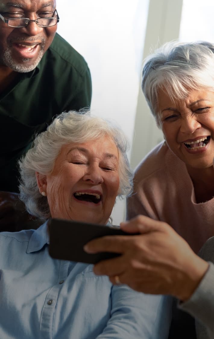 a group of senior laughing while watching content on a mobile device